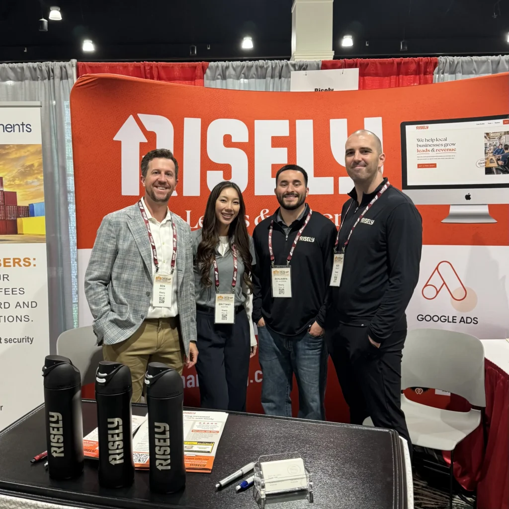 Four Risely team members in branded apparel posing at their conference booth promoting growth services for local businesses, with Google Ads partnership signage visible.