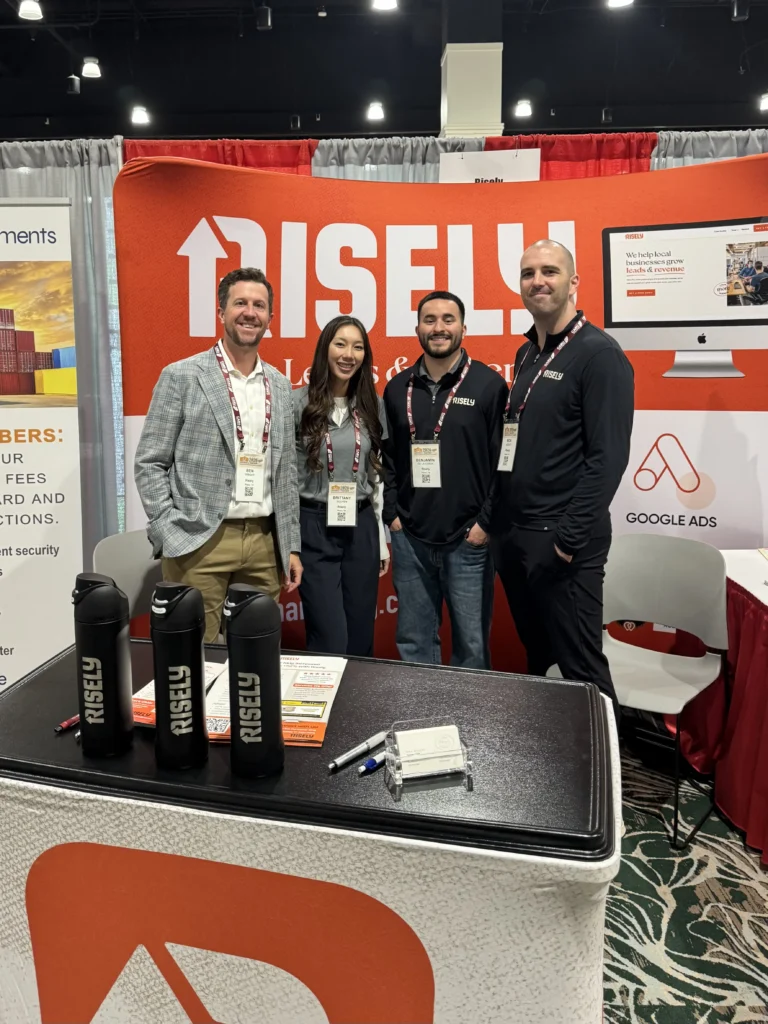 Four Risely team members in branded apparel posing at their conference booth promoting growth services for local businesses, with Google Ads partnership signage visible.